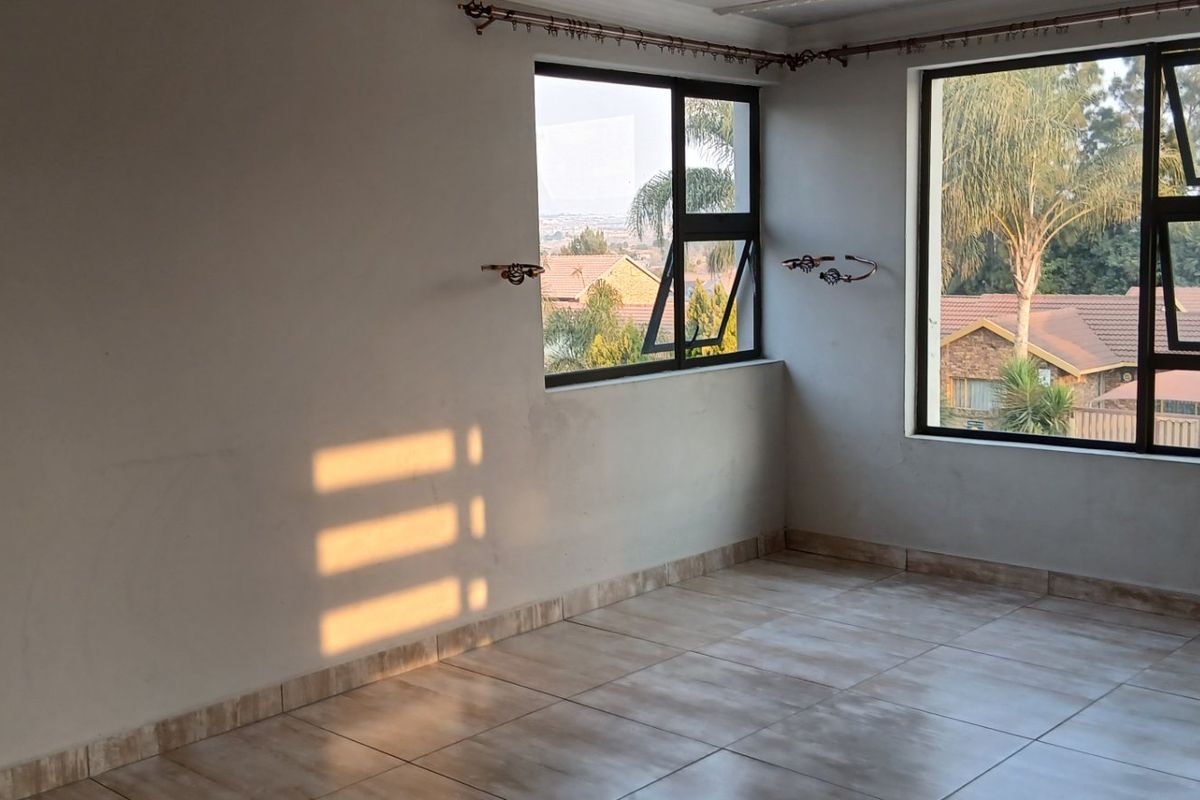 An empty living area featuring tiled flooring and large aluminium-framed windows that provide ample natural light and views of the surrounding neighbourhood.