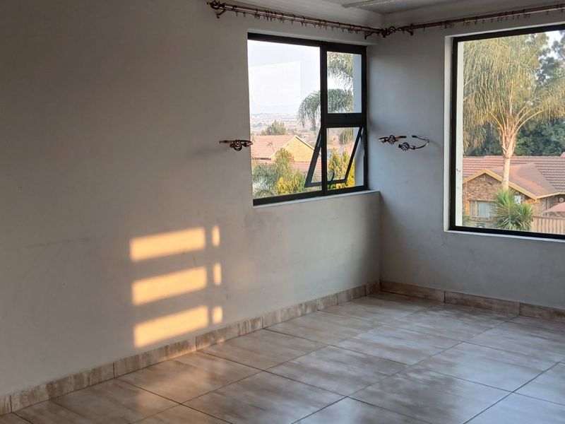 An empty living area featuring tiled flooring and large aluminium-framed windows that provide ample natural light and views of the surrounding neighbourhood.