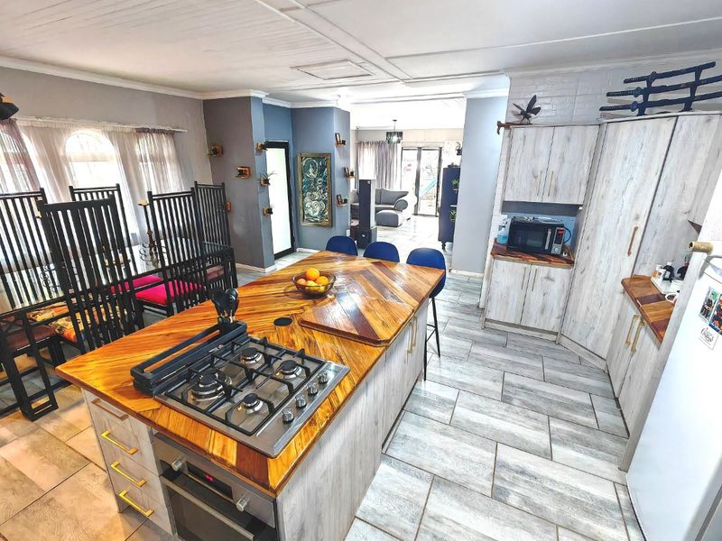 Spacious open-plan kitchen and dining area featuring a central island with a built-in gas hob, oven, and modern tiled flooring throughout.