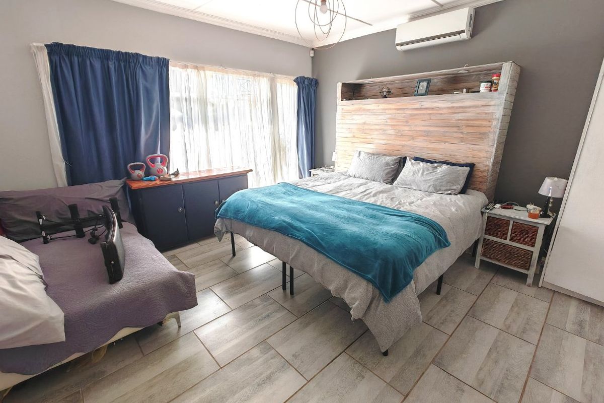 A bedroom featuring tiled flooring, a wall-mounted air conditioning unit, and a custom built-in wooden headboard with integrated shelving.