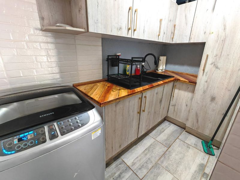 A functional laundry area featuring modern wood-look cabinetry, a durable wooden countertop, an undermount sink, and stylish brick-patterned wall finishes.