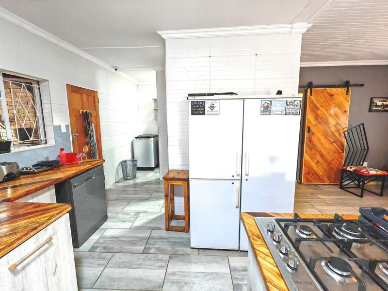 A functional kitchen featuring wooden countertops, a gas hob, tiled flooring, and a rustic barn door leading to adjacent living spaces.