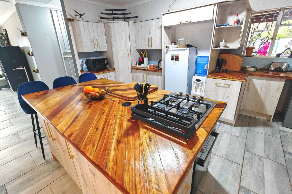 A functional kitchen featuring a large wooden island with an integrated gas hob, built-in oven, and ample cabinetry with light wood finishes.