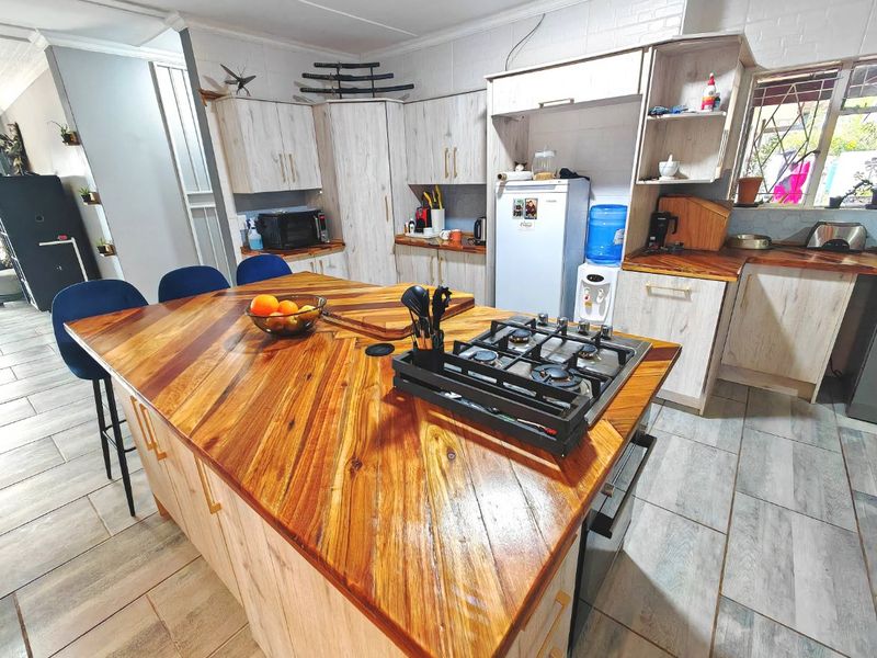 A functional kitchen featuring a large wooden island with an integrated gas hob, built-in oven, and ample cabinetry with light wood finishes.