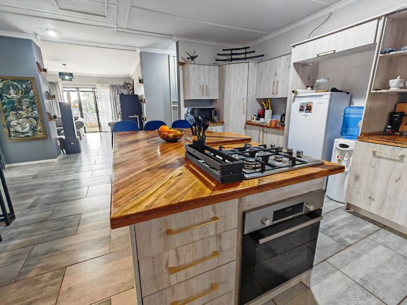 Open plan kitchen featuring a central island with a gas cooktop, built-in oven, wooden countertop, and modern cabinetry, flowing into the adjacent living area.