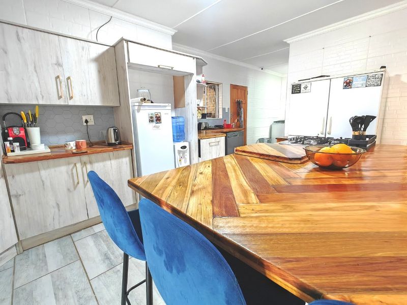 A functional kitchen featuring light wood-look cabinetry, a large wooden breakfast island, gas hob, and tiled flooring with a modern backsplash.