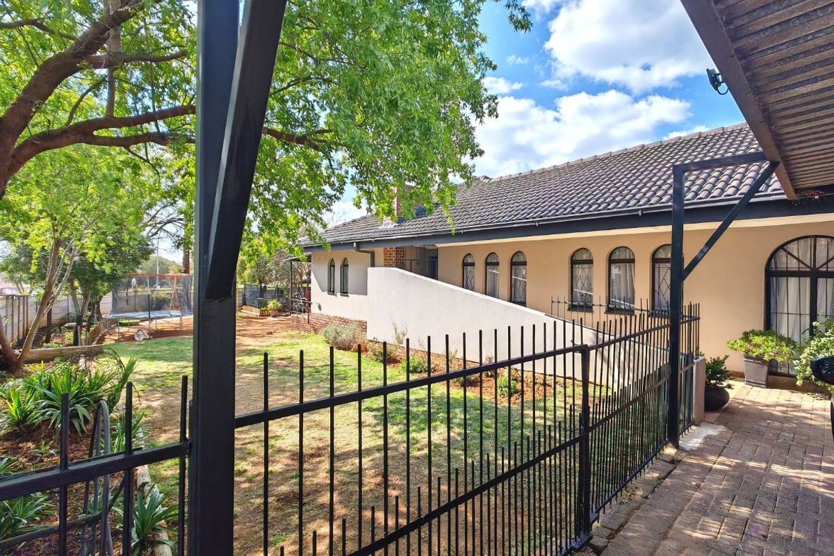 A view of the rear exterior featuring a paved patio, wrought iron fencing, and a well-maintained garden with arched windows along the building facade.