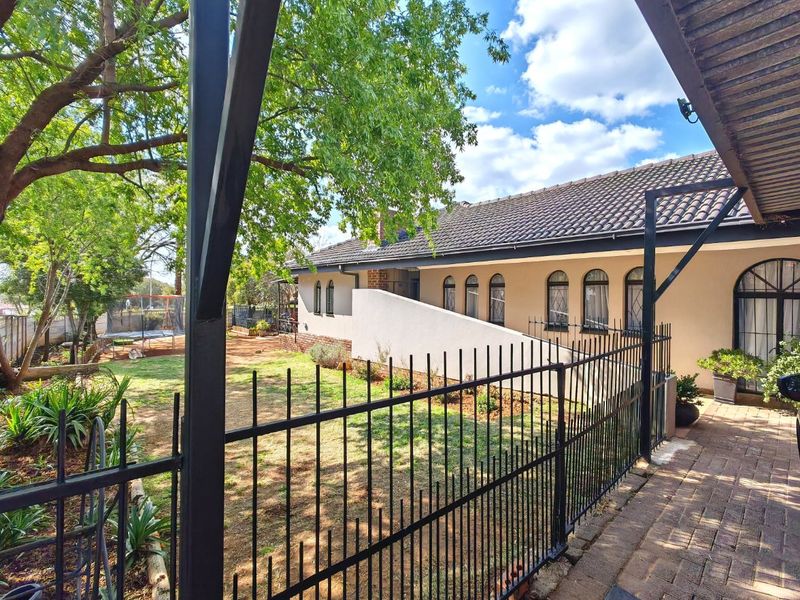 A view of the rear exterior featuring a paved patio, wrought iron fencing, and a well-maintained garden with arched windows along the building facade.