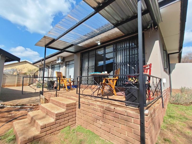A raised brick patio featuring a corrugated roof, metal security gate, and sliding glass doors, providing a functional outdoor living space.