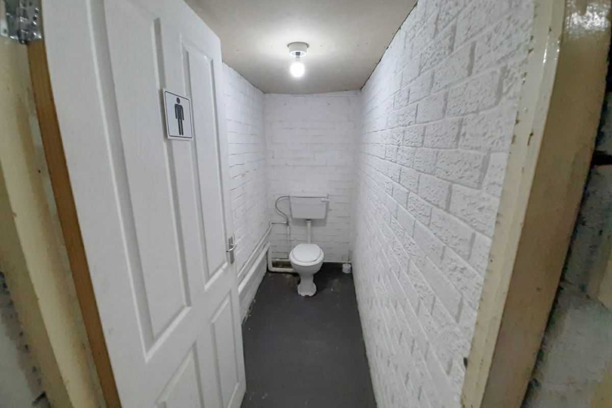 A functional industrial-style restroom featuring painted brick walls, a standard toilet, and basic utility lighting.