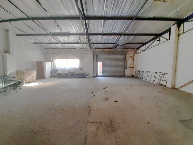 Spacious industrial utility area featuring exposed steel roof trusses, foil insulation, concrete flooring, and a secure roller shutter door access point.