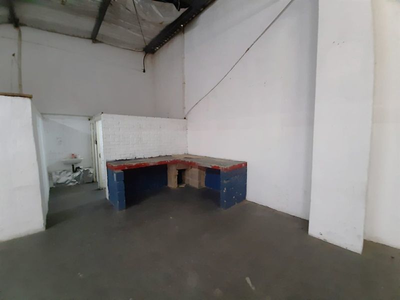 Industrial utility space featuring a concrete floor, built-in masonry workbench, and a wall-mounted basin, suitable for workshop or storage use.