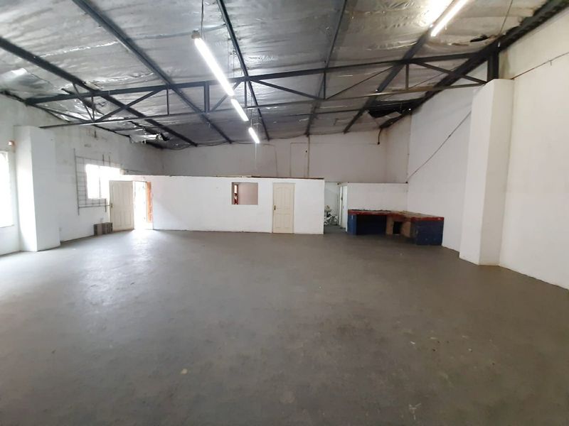 Spacious industrial utility area featuring exposed steel roof trusses, concrete flooring, and a partitioned office section, suitable for various commercial or storage applications.
