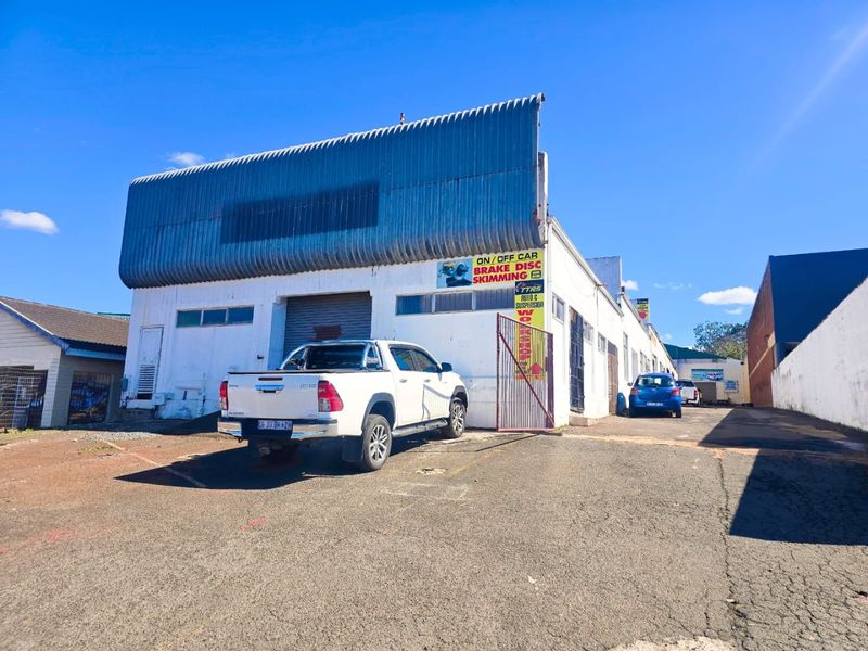 Front elevation of an industrial property featuring a corrugated metal roof, roller shutter access, and paved driveway area.
