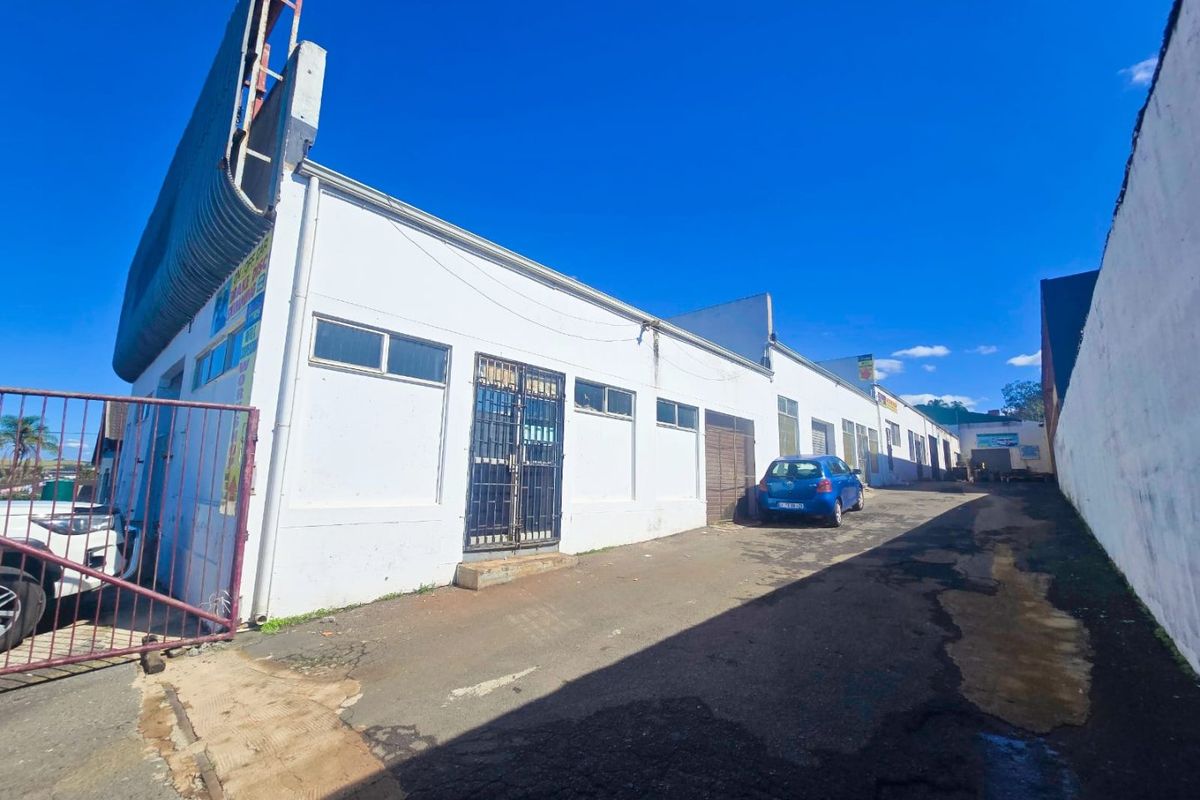 Industrial property exterior featuring a long asphalt driveway, white facade, and security gates, showing signs of wear and aging.