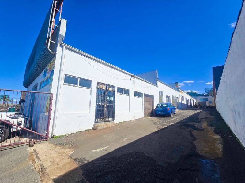 Industrial property exterior featuring a long asphalt driveway, white facade, and security gates, showing signs of wear and aging.