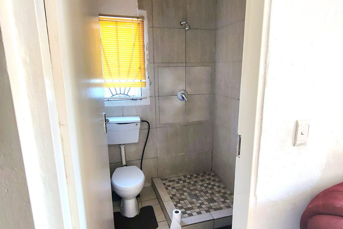 Compact bathroom featuring a shower, toilet, and tiled finishes. The space requires cosmetic updates to the wall tiling and general maintenance.