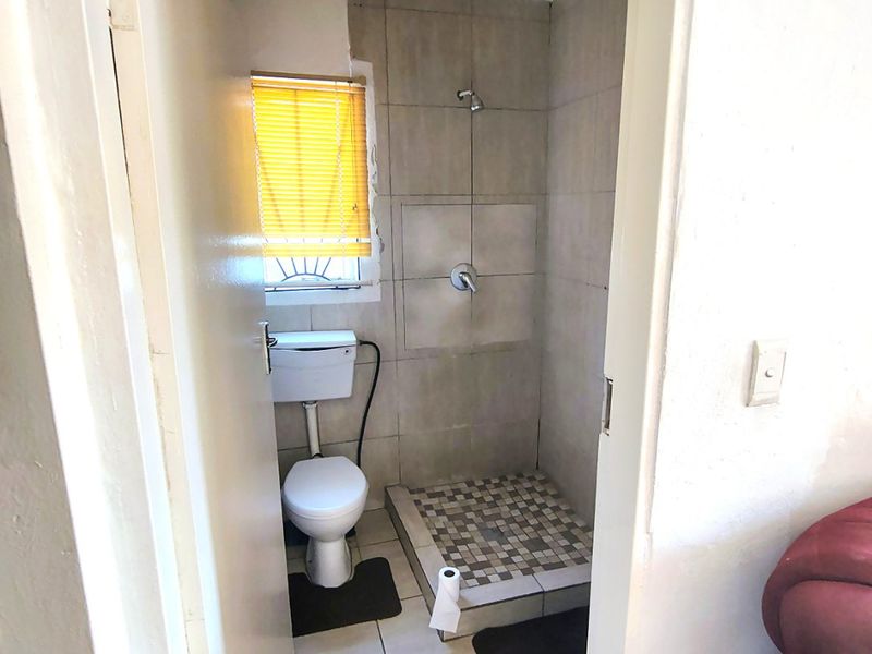 Compact bathroom featuring a shower, toilet, and tiled finishes. The space requires cosmetic updates to the wall tiling and general maintenance.