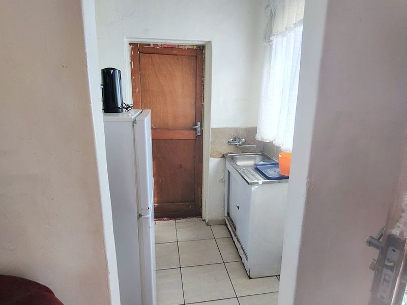 A compact scullery area featuring tiled flooring, a stainless steel sink, and direct access to an exterior timber door.