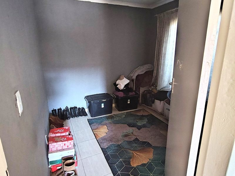 A small bedroom featuring tiled flooring and neutral grey walls, currently utilized as a storage space.