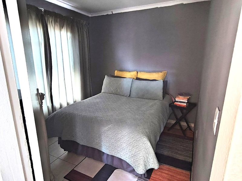 A compact bedroom featuring tiled flooring and neutral wall finishes, offering a functional space with natural light from the window.