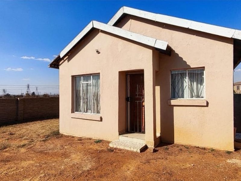 Front view of a detached house featuring a simple facade, security gate, burglar bars, and an unlandscaped yard enclosed by a perimeter wall.