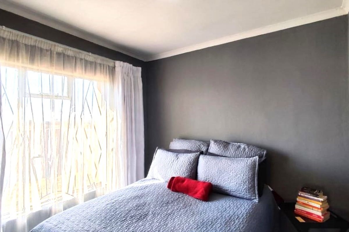 A well-maintained bedroom featuring neutral grey walls, coving, and a large window allowing for natural light.