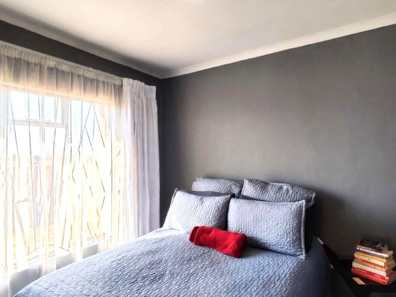 A well-maintained bedroom featuring neutral grey walls, coving, and a large window allowing for natural light.