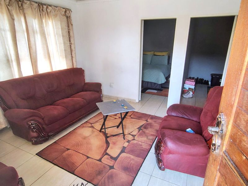 A living room featuring tiled flooring and direct access to adjacent bedrooms, requiring cosmetic updates to the ceiling and wall finishes.