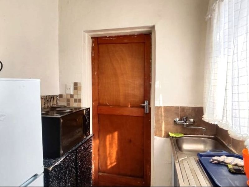 A compact scullery area featuring a stainless steel sink, tiled splashback, and a wooden door, providing functional utility space.