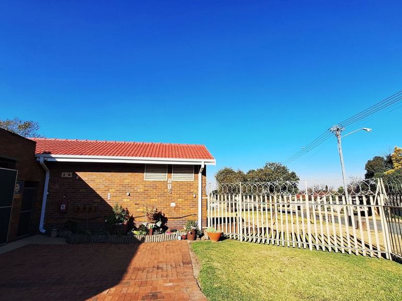Rear exterior view of the property featuring brick paving, a secure perimeter fence with razor wire, and a tiled roof structure.