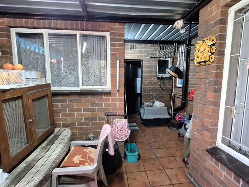 A covered outdoor patio area featuring exposed brick walls, tiled flooring, and a corrugated metal roof, providing a functional sheltered space.