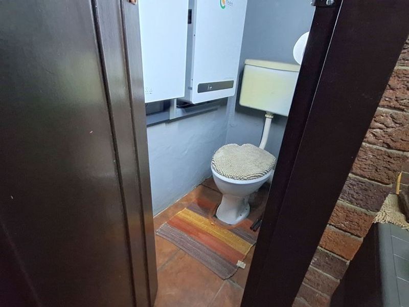 A small bathroom featuring a toilet and wall-mounted inverter system, finished with exposed brickwork and tiled flooring.