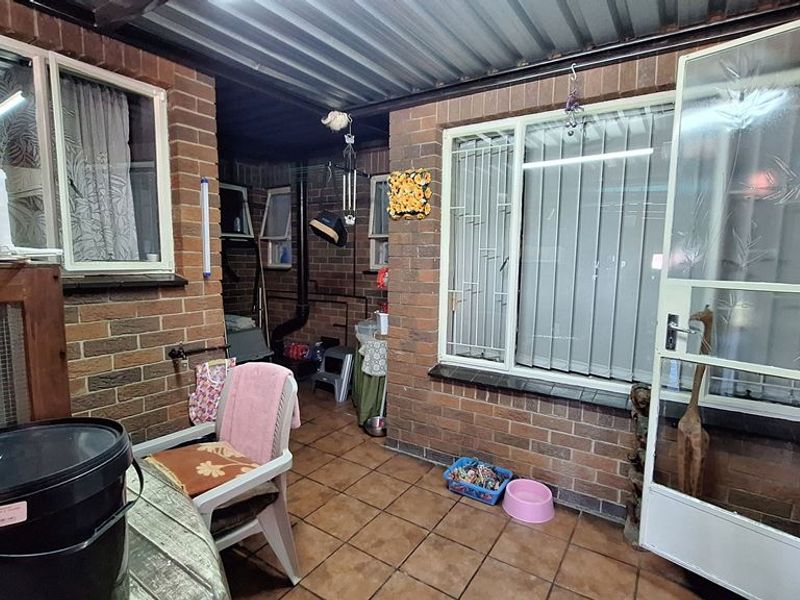 A covered outdoor patio area featuring exposed brick walls, tiled flooring, and a corrugated metal roof, providing a functional transition space.