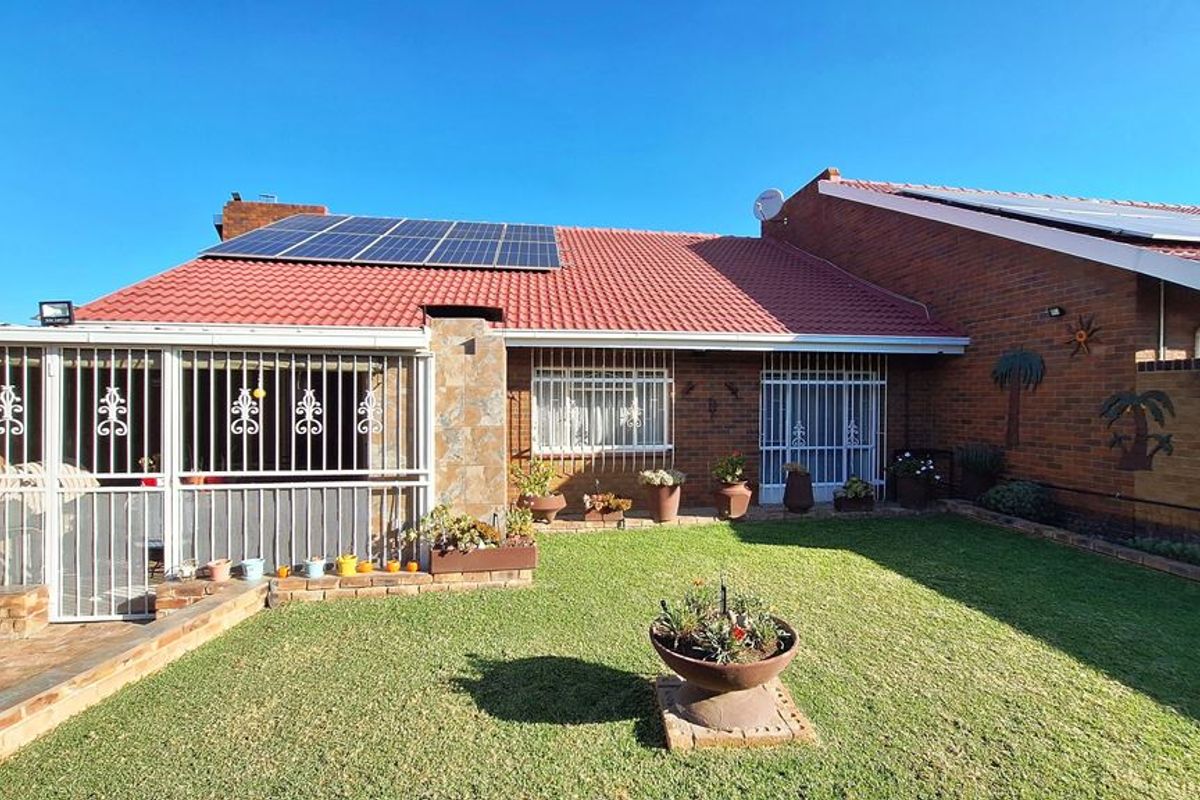 Rear view of the property featuring a brick facade, tiled roof with solar panels, an enclosed patio area, and a well-maintained lawn.