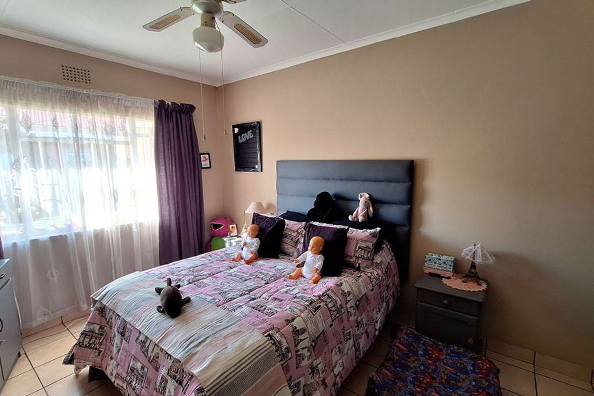 A bedroom featuring tiled flooring, a ceiling fan, and large windows with curtain rails, providing a functional and well-lit living space.
