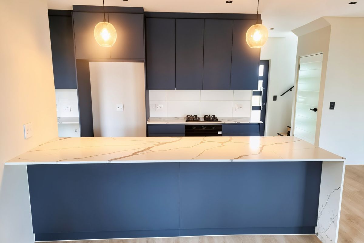 Modern kitchen featuring dark blue cabinetry, a large stone-topped island, built-in oven, gas hob, and contemporary pendant lighting.