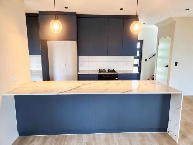 Modern kitchen featuring dark blue cabinetry, a large stone-topped island, built-in oven, gas hob, and contemporary pendant lighting.