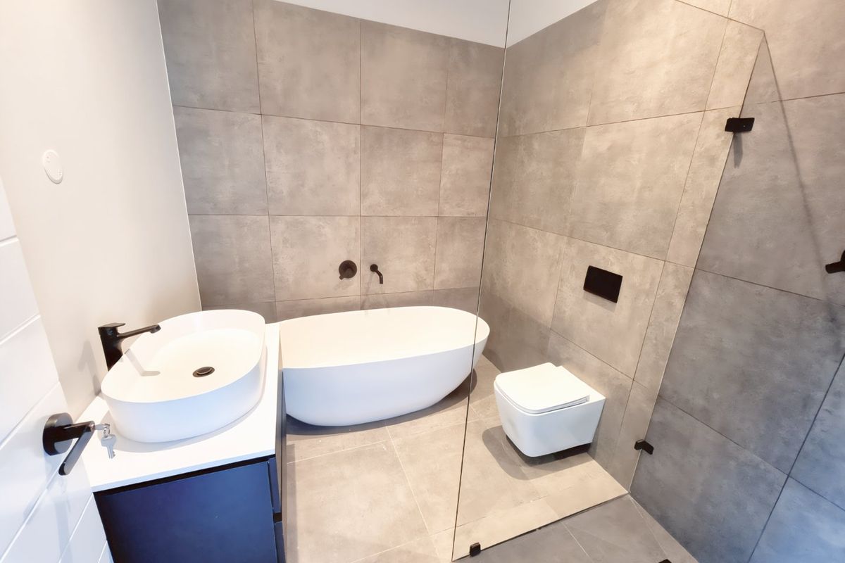 Modern bathroom featuring a freestanding bathtub, wall-mounted toilet, vessel sink on a vanity cabinet, and a glass shower screen with matte black fixtures.