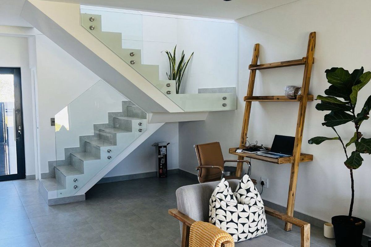 Modern living area featuring a contemporary staircase with glass balustrades and sleek tiled flooring, creating a bright and open atmosphere.