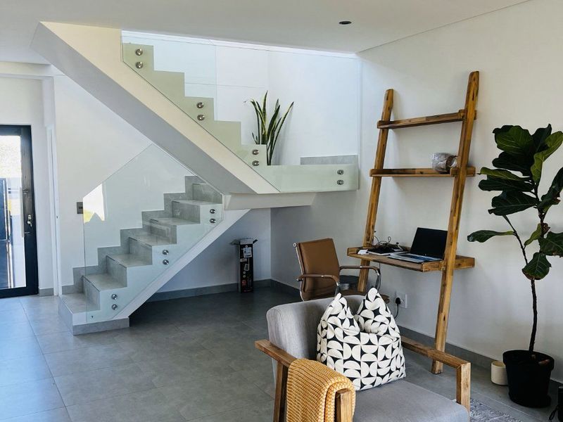 Modern living area featuring a contemporary staircase with glass balustrades and sleek tiled flooring, creating a bright and open atmosphere.