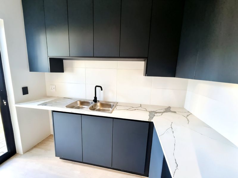 Modern kitchen featuring dark matte cabinetry, white marble-look stone countertops, a double bowl sink with a black mixer tap, and clean tiled splashbacks.