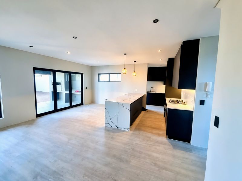 Modern open-plan kitchen and living area featuring a stone-topped island, sleek black cabinetry, gas cooktop, and large sliding doors leading to the patio.
