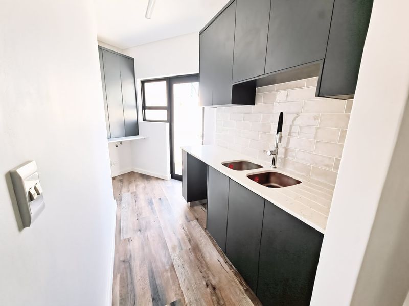 Modern scullery featuring dark cabinetry, stone countertops, a double sink with mixer tap, and subway tile backsplash, providing a clean and functional prep area.