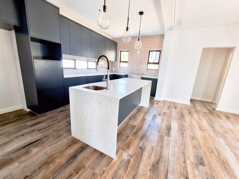 Modern kitchen featuring dark cabinetry, a white quartz island with an undermount sink, subway tile backsplash, and wood-look flooring.
