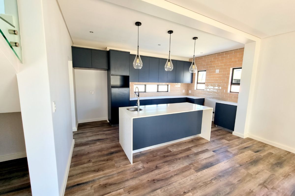 Modern kitchen featuring dark cabinetry, a central island with stone countertops, subway tile backsplash, and wood-look laminate flooring in an open-plan layout.