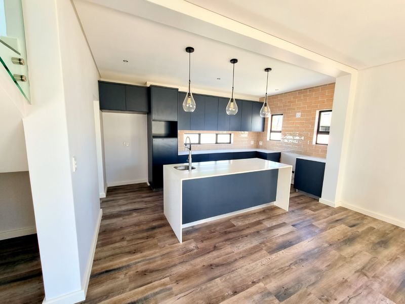 Modern kitchen featuring dark cabinetry, a central island with stone countertops, subway tile backsplash, and wood-look laminate flooring in an open-plan layout.