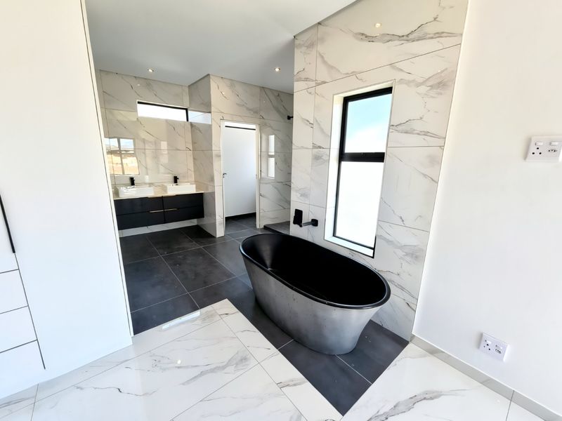 Modern, high-end bathroom featuring a sleek freestanding bathtub, double vanity with black fixtures, and elegant marble-look wall tiling.