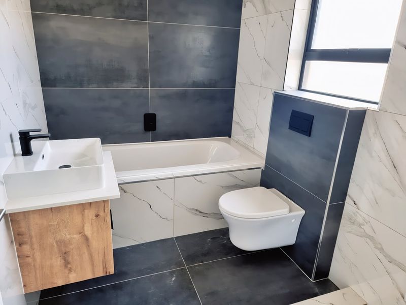 Modern bathroom featuring a wall-mounted toilet, built-in bathtub, and a contemporary vanity with a vessel sink, finished with stylish contrasting porcelain tiles.