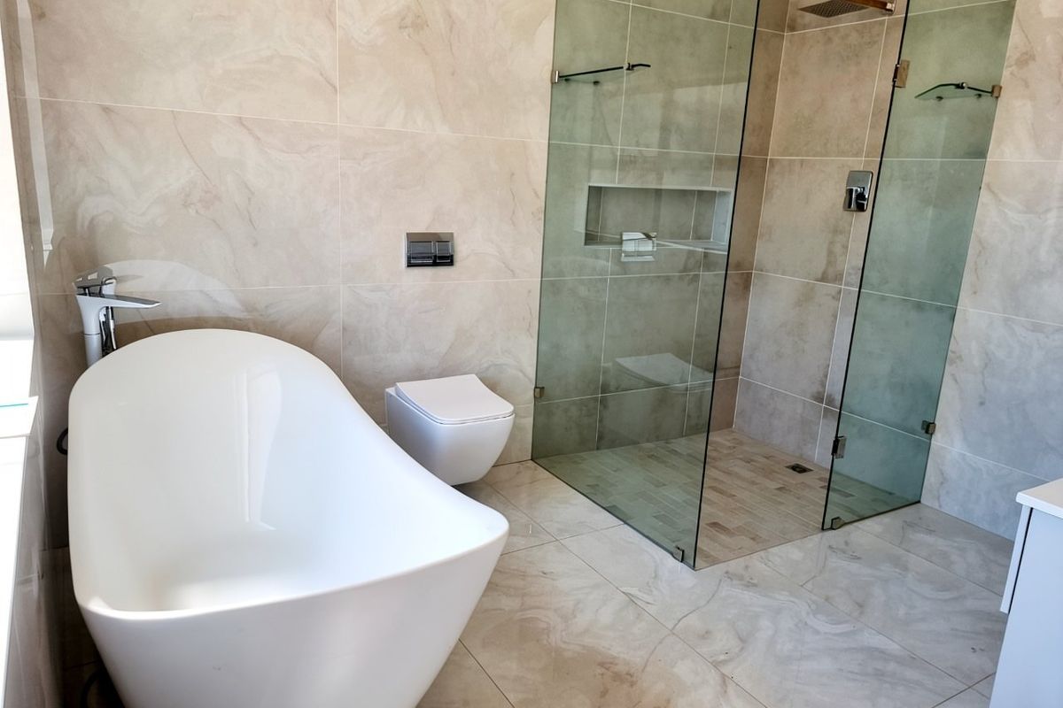Modern bathroom featuring a sleek freestanding bathtub, wall-hung toilet, and a spacious frameless glass walk-in shower with neutral stone-look tiling.